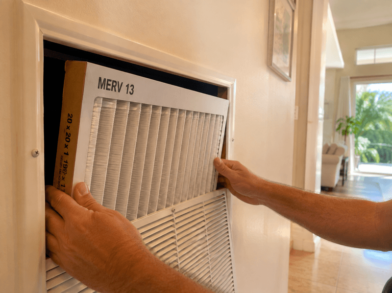Homeowner installing a MERV 13 pleated air filter in a hallway return vent during a smoke event.