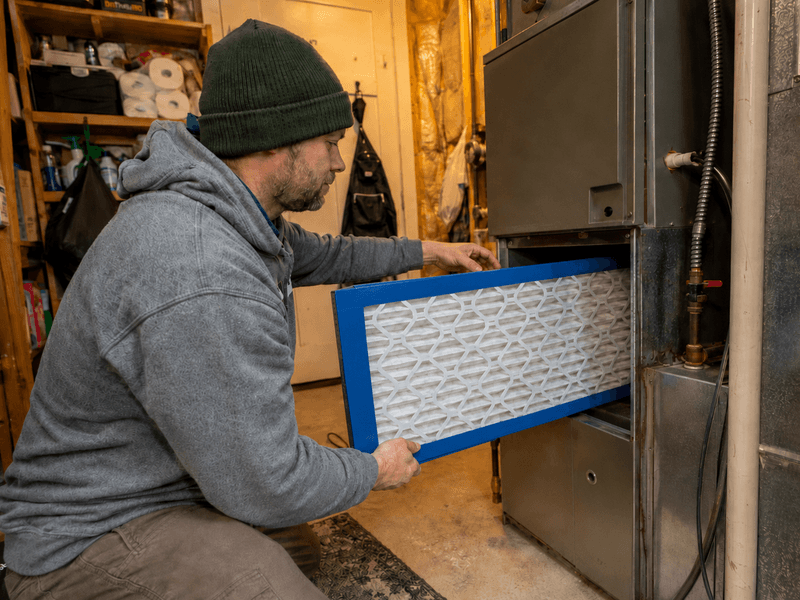 Homeowner installing a Filterbuy MERV 13 air filter during Alaska wildfire smoke season.